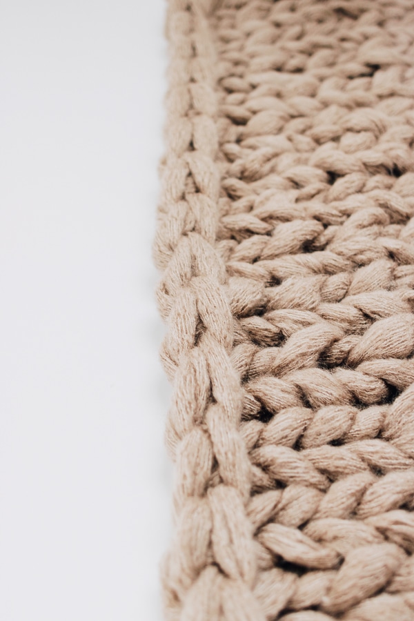 a close up of a chunky knit blanket, tan/beige colored with white background