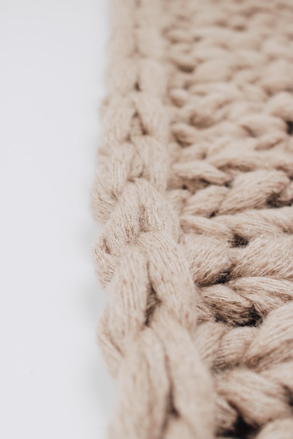 a close up of a chunky knit blanket, tan/beige colored with white background