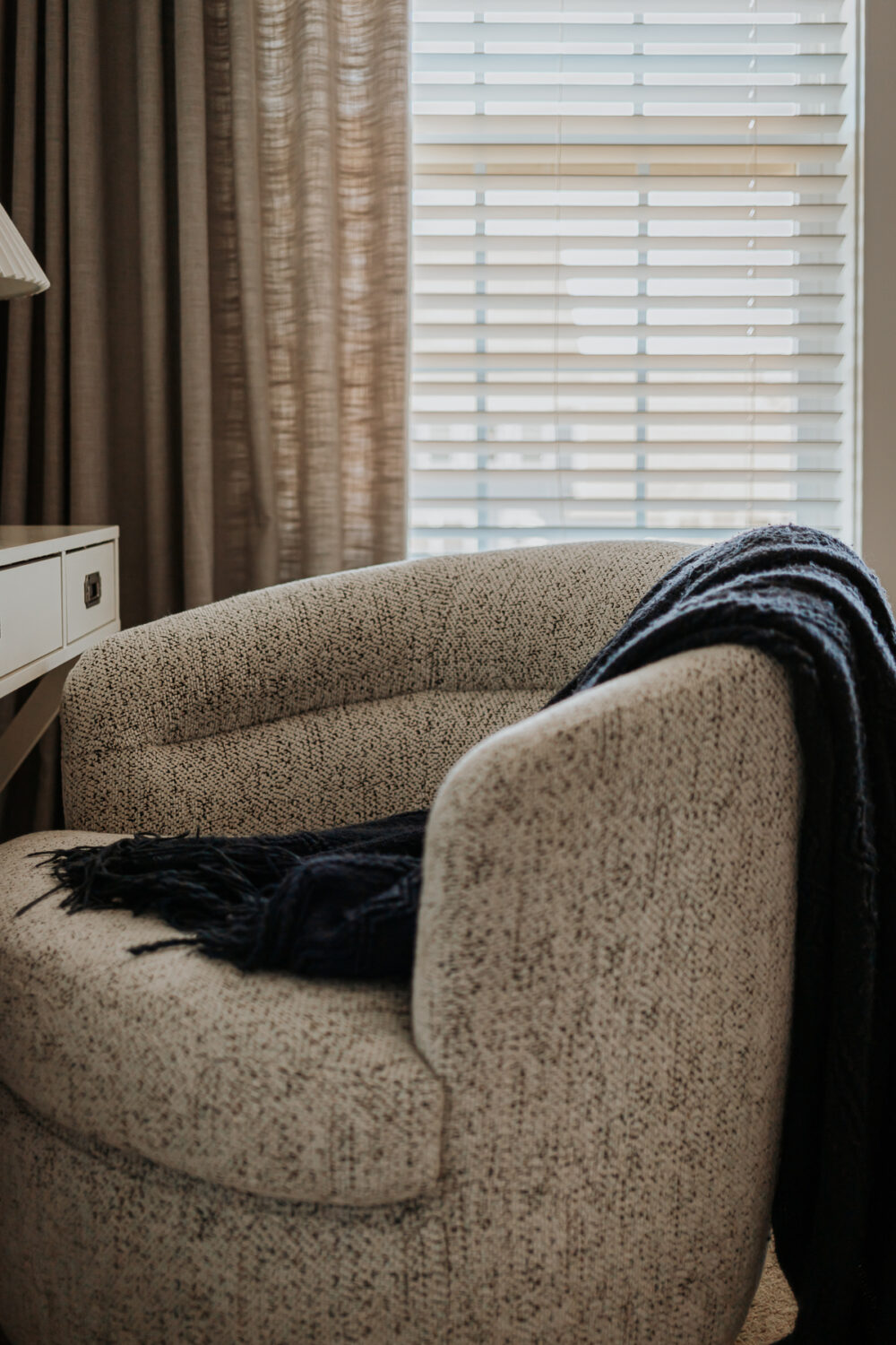 close up view of boucle accent chairs with a navy blanket on it and window behind it