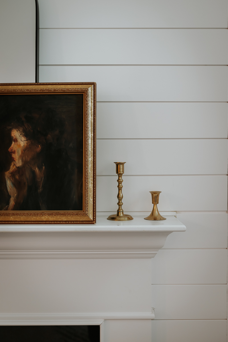 thrifted gold candlesticks on a fireplace mantel next to a framed picture