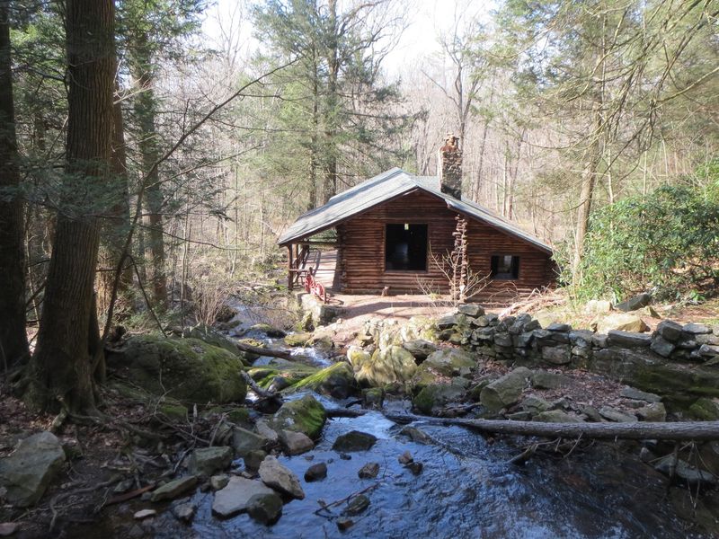 A Log Cabin And A Waterfall Waiting In The Woods