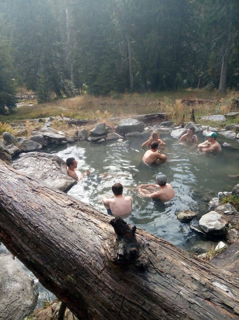 Steaming Water Spills Into A Riverside Pool You Reach By Footbridge In Idaho's Lochsa Country - Decor Hint Crowds, Company, And Clothing Choices